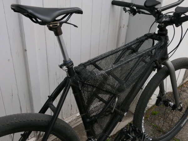 vue de face zoomée sur d'un vélo de voyage noir avec filet de pêche dans le triangle avant. le fond est un garage avec des portes blanches / "Vélo de bikepacking ninja tout-terrain noir"